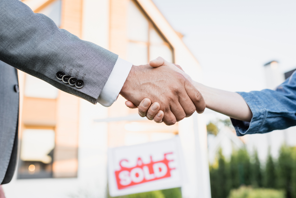 Cropped view of broker nad woman shaking hands with blurred sign with sold lettering on background